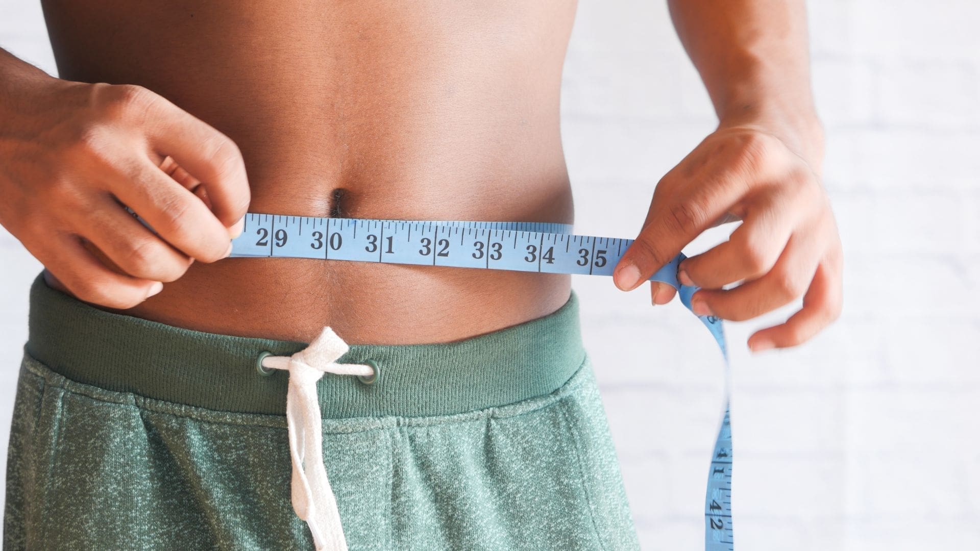 Person measuring waist circumference with a tape measure, illustrating results of CoolSculpting for belly fat reduction and body contouring.