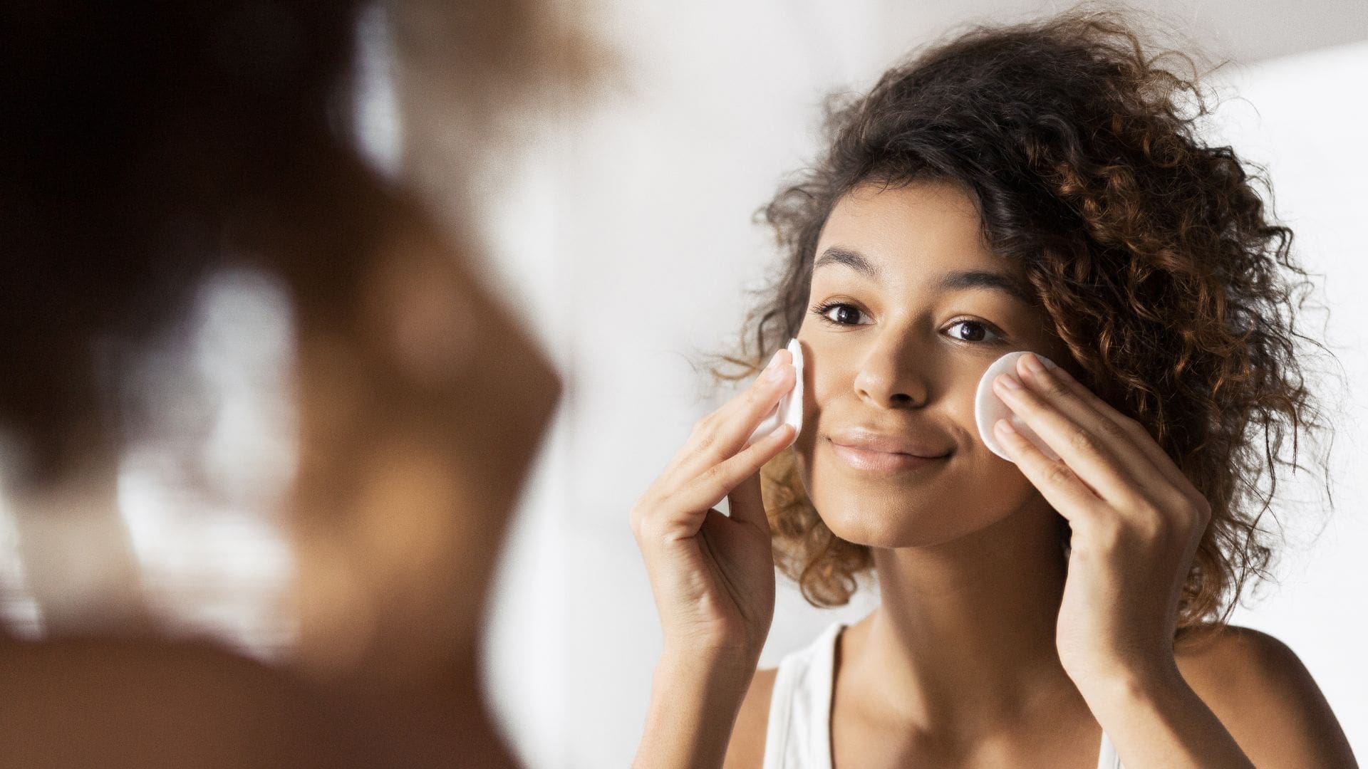 Young woman applying skincare product with cotton pad, reflecting the importance of aftercare following acne treatment facials for improved skin clarity and texture.