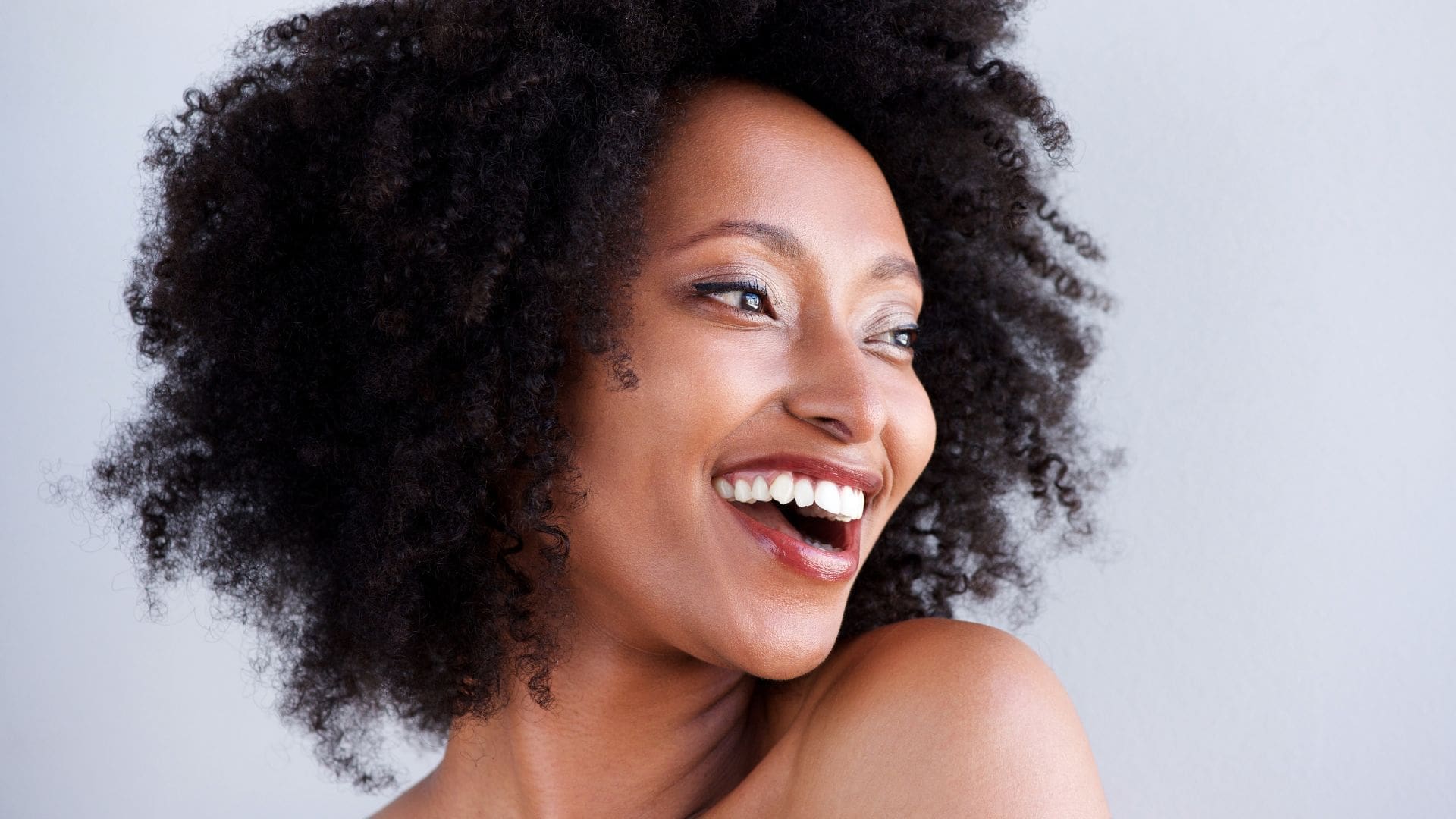 Smiling woman with curly hair showcasing youthful skin, representing the benefits of Botox for wrinkle reduction and aesthetic enhancement.