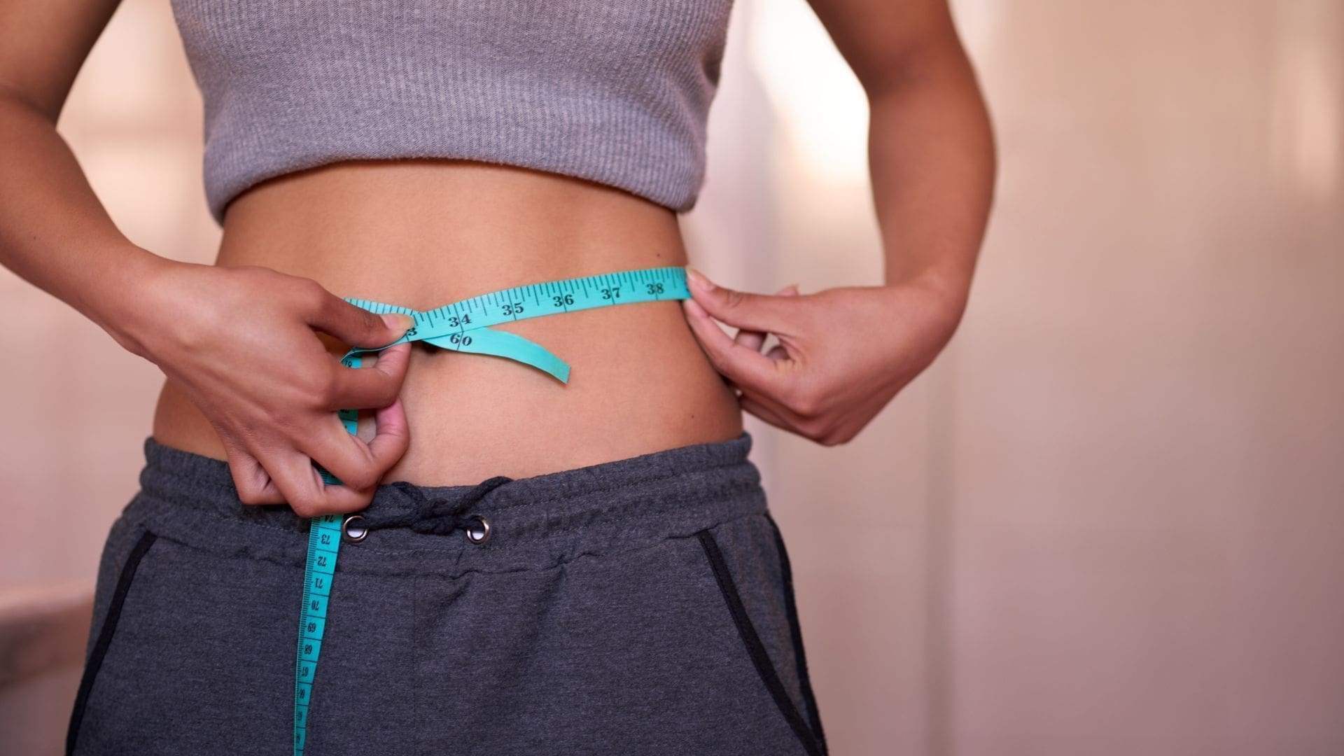 Woman measuring waist with a tape measure, illustrating body contouring and fat reduction concepts relevant to CoolSculpting treatments in Towson, MD.