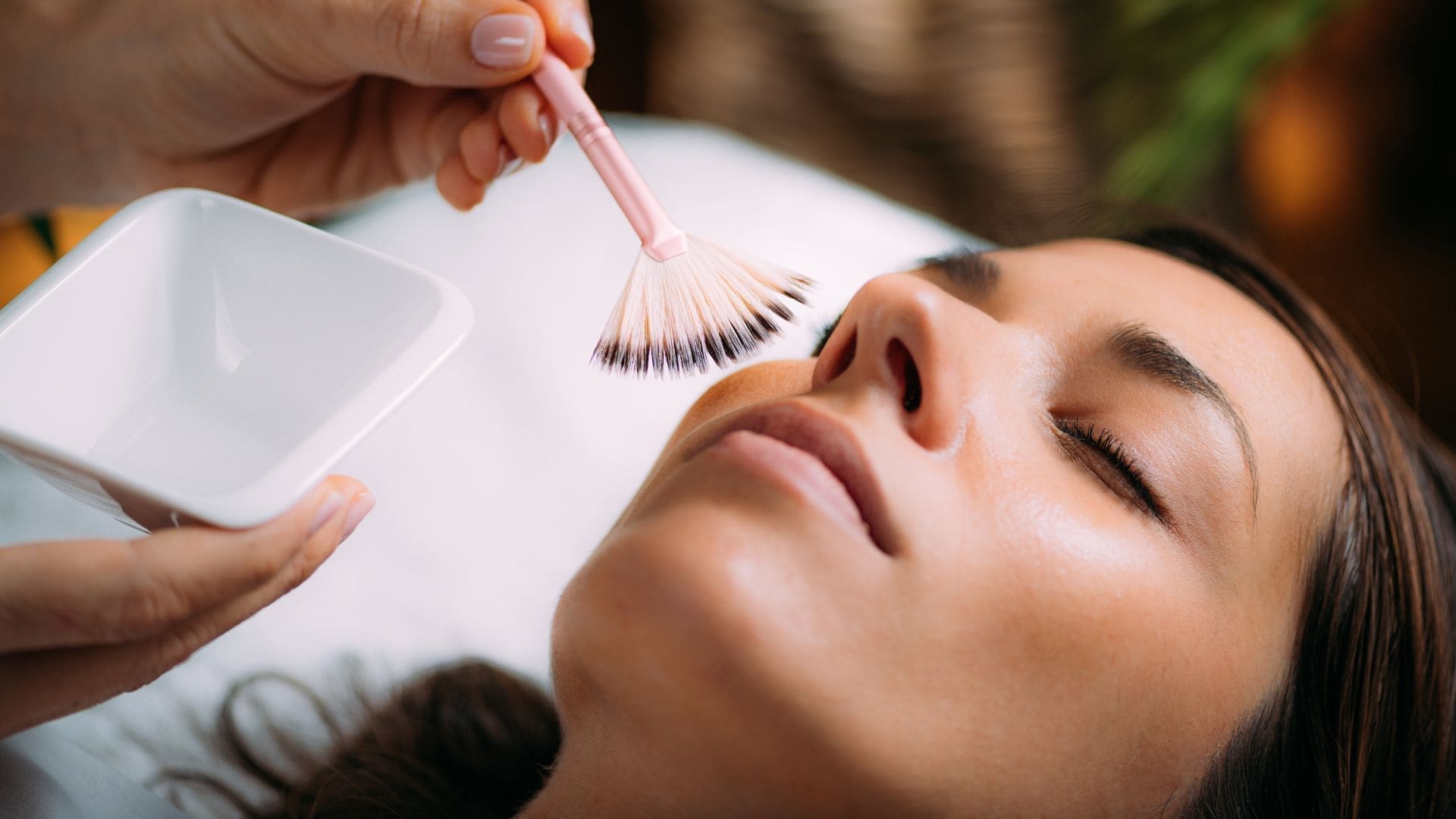 Woman receiving a chemical peel treatment with a brush, showcasing skincare application in a spa setting, emphasizing skin rejuvenation and aesthetic services.