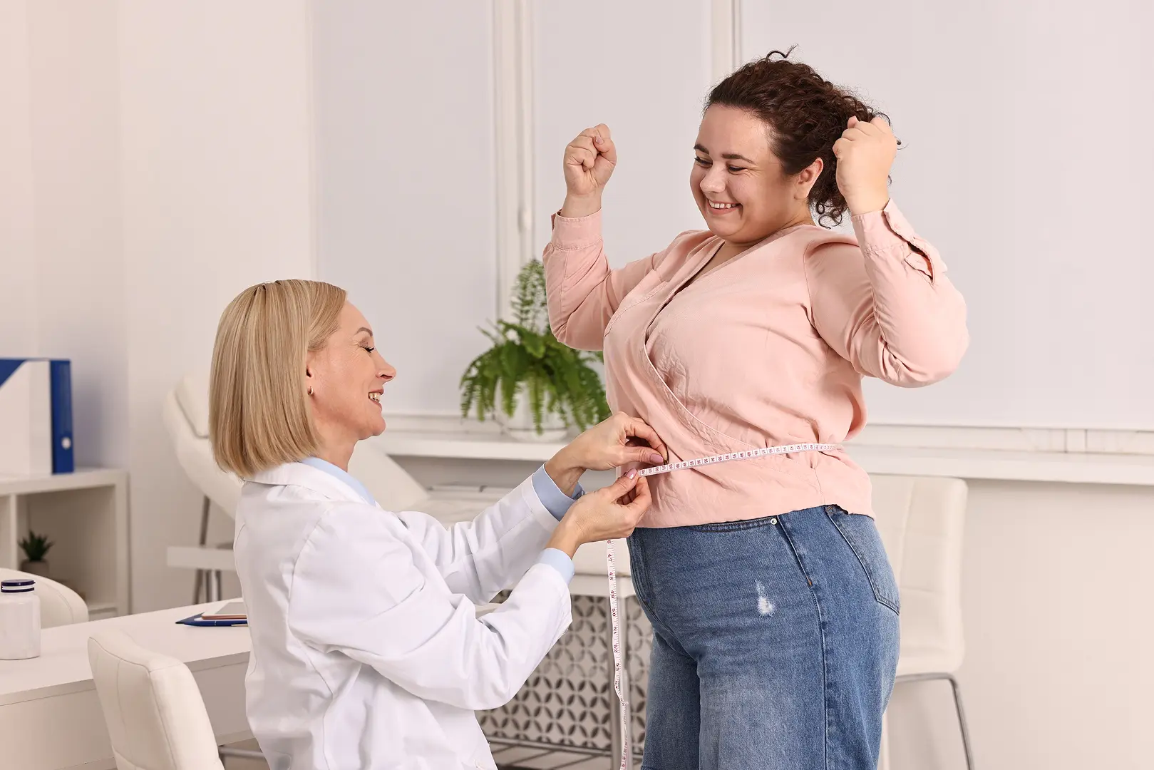 A woman happily tries on a pink jacket with help from a stylist.