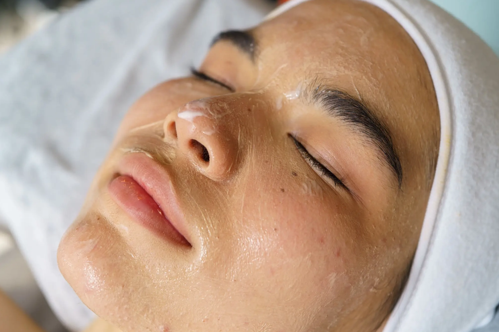 Close-up of a woman receiving a facial treatment with a creamy mask applied.