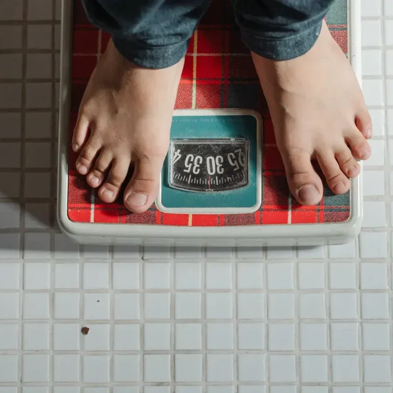 Person standing on a red weighing scale showing weight.
