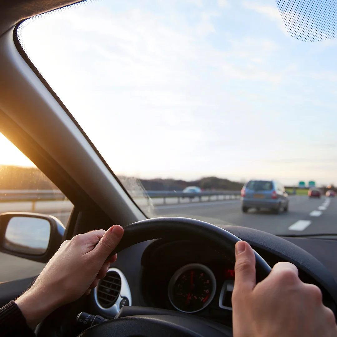 Person driving a car on a highway during sunset.
