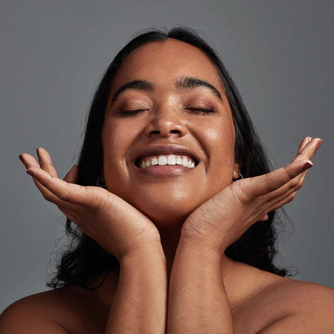 A woman joyfully smiles with hands framing her face.