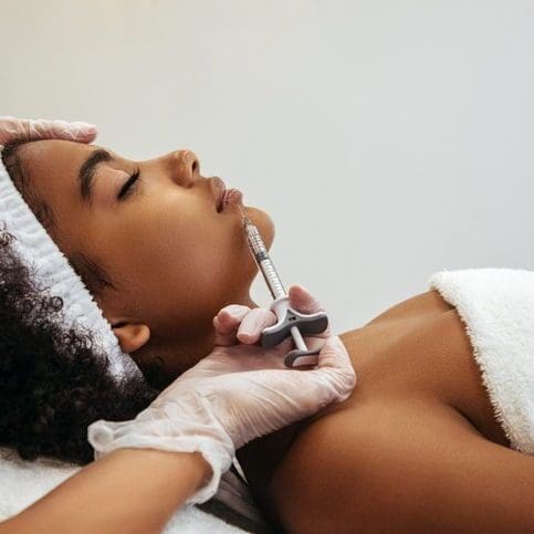 Woman receiving a facial treatment with a handheld device.