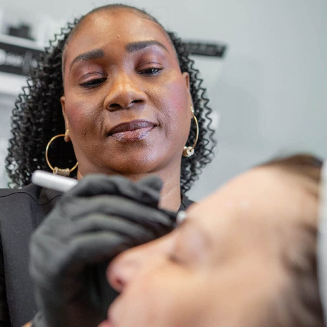 A professional beautician applies makeup to a client's face in a close-up shot.