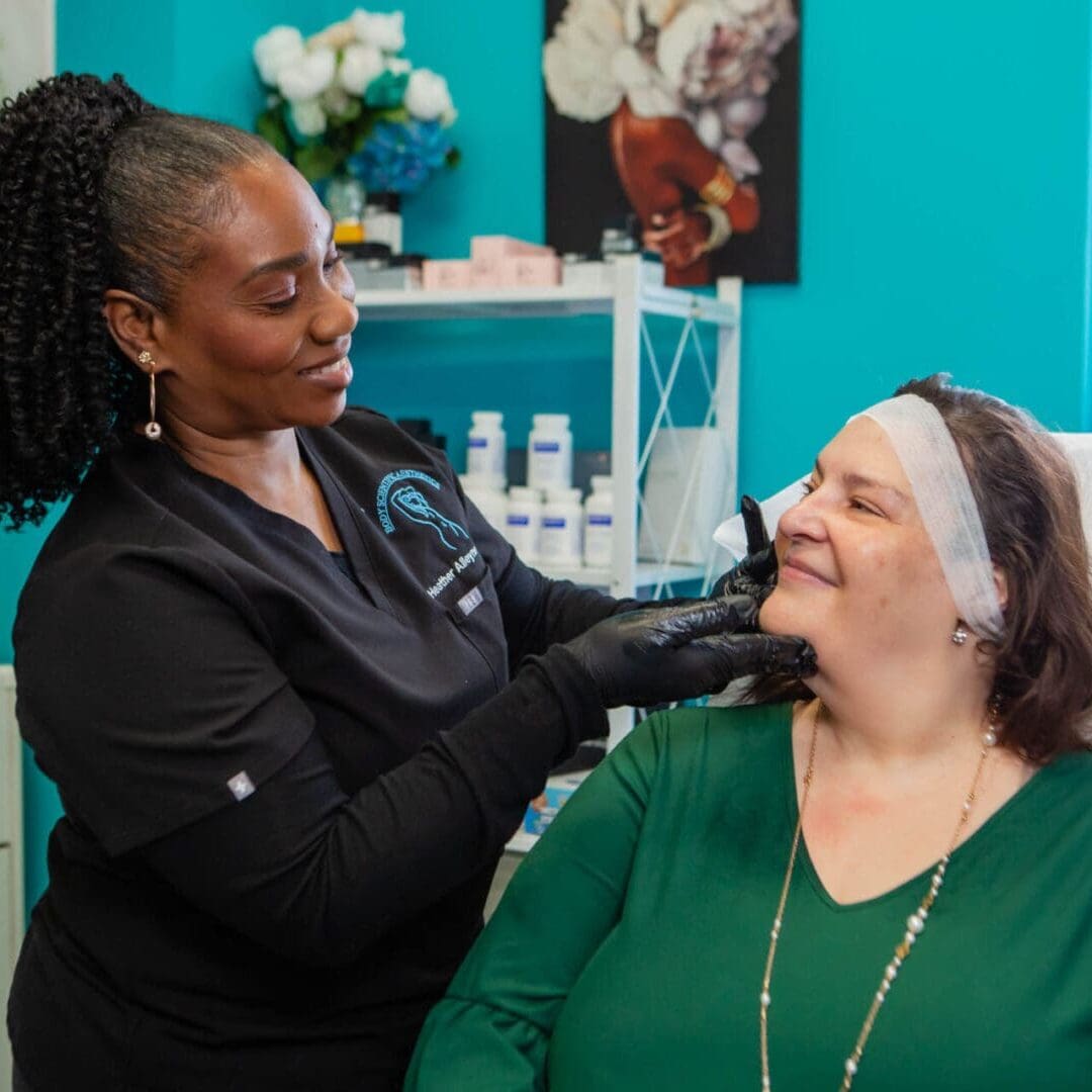 A skincare professional examines a smiling woman's face in a bright clinic.