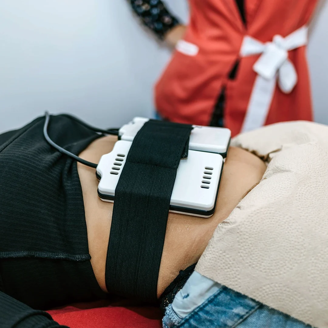 Woman undergoing a body contouring treatment with a device strapped to her abdomen.