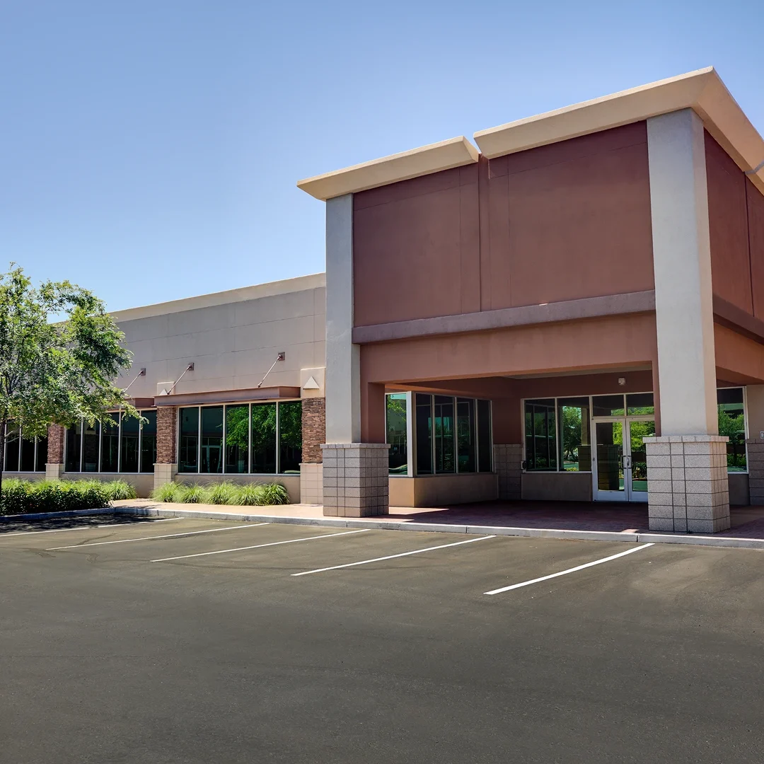 Modern commercial building with large windows and a parking area.